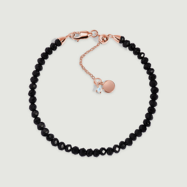A black obsidian bracelet with rose gold vermeil fittings is centered on a pale gray surface.