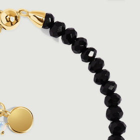 A yellow gold vermeil end cap meets a curved row of glossy faceted black obsidian beads.