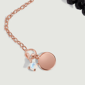 Rose gold vermeil extender links end in a round charm beside a small pale gemstone.