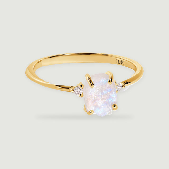 A yellow gold ring holds a rough white moonstone between two small round diamond accents.