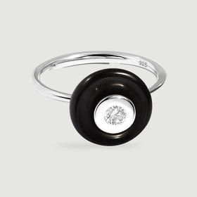 The sterling silver ring has a glossy black circular stone around a clear round center on a light gray surface.