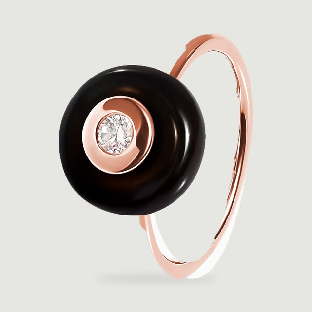 The rose gold ring stands at an angle with its circular black top projecting above the narrow band.