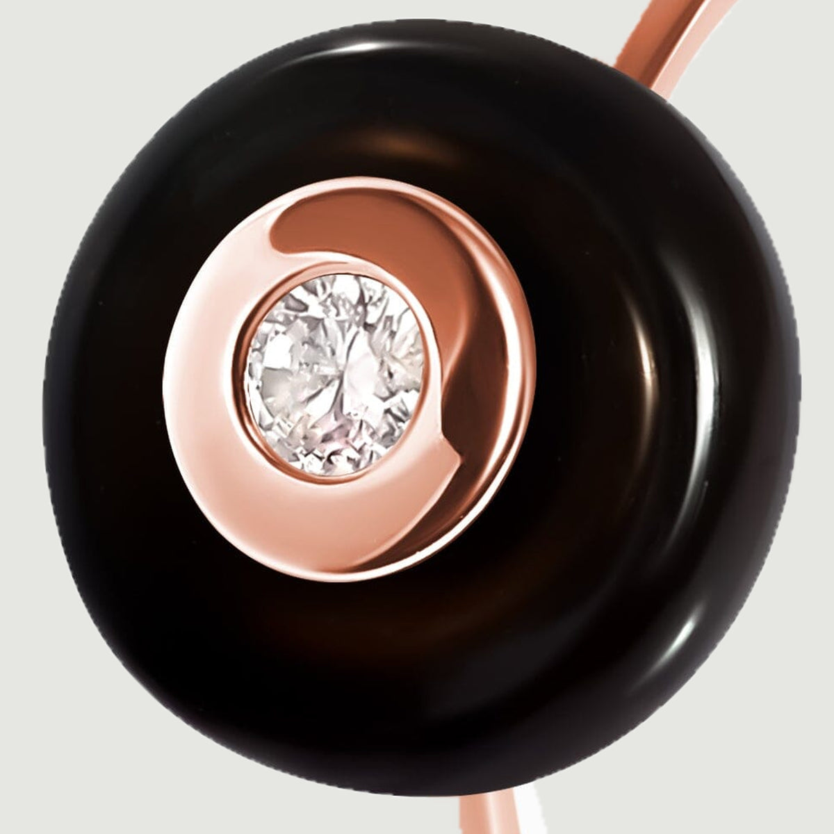 The glossy black stone surrounds a bright rose gold bezel and a round clear gemstone in this close view.