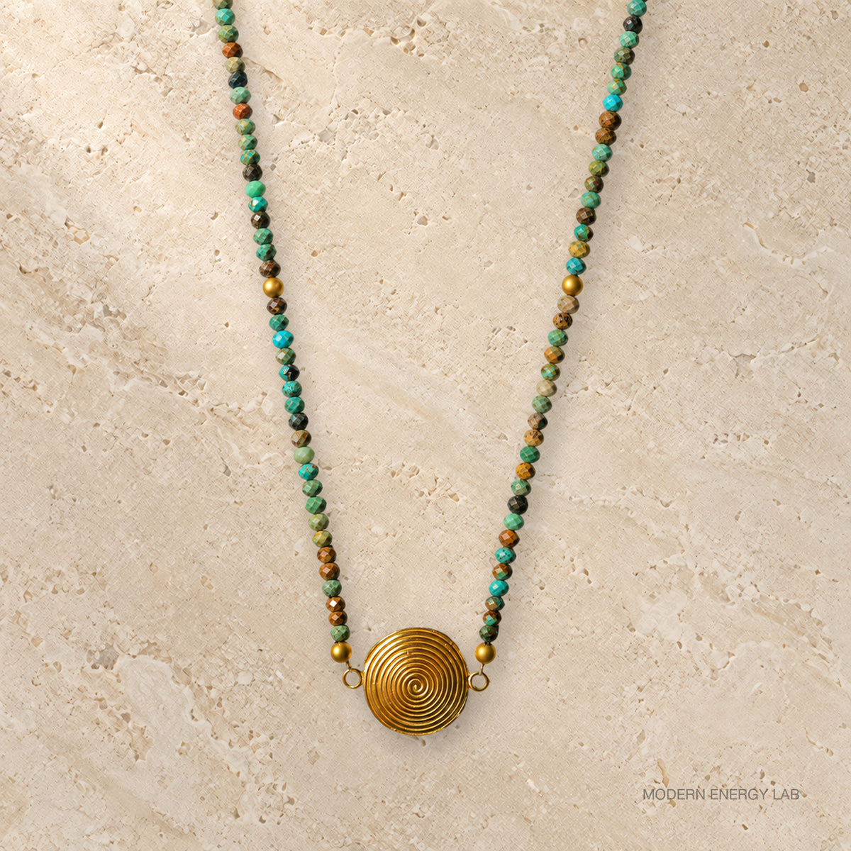 Turquoise beaded necklace with gold-tone spiral pendant on warm stone