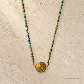 Turquoise beaded necklace with gold-tone spiral pendant on warm stone