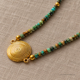 Real close view of the raised spiral pendant and faceted turquoise beads on linen