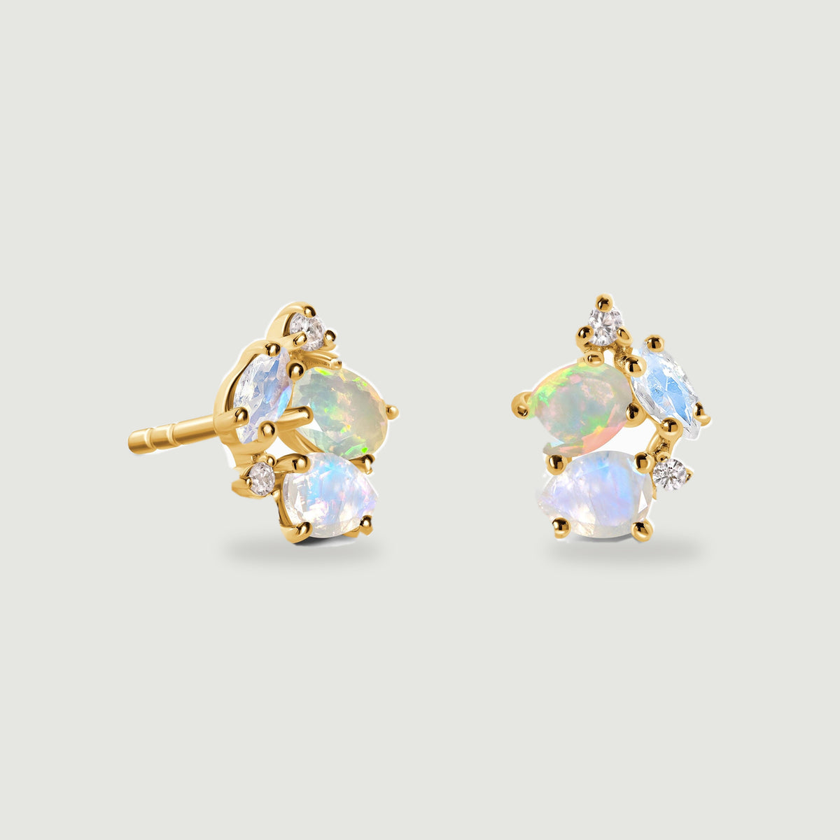Two yellow gold vermeil stud earrings show an iridescent opal, pale blue moonstones, and small clear accent stones on a light gray background.