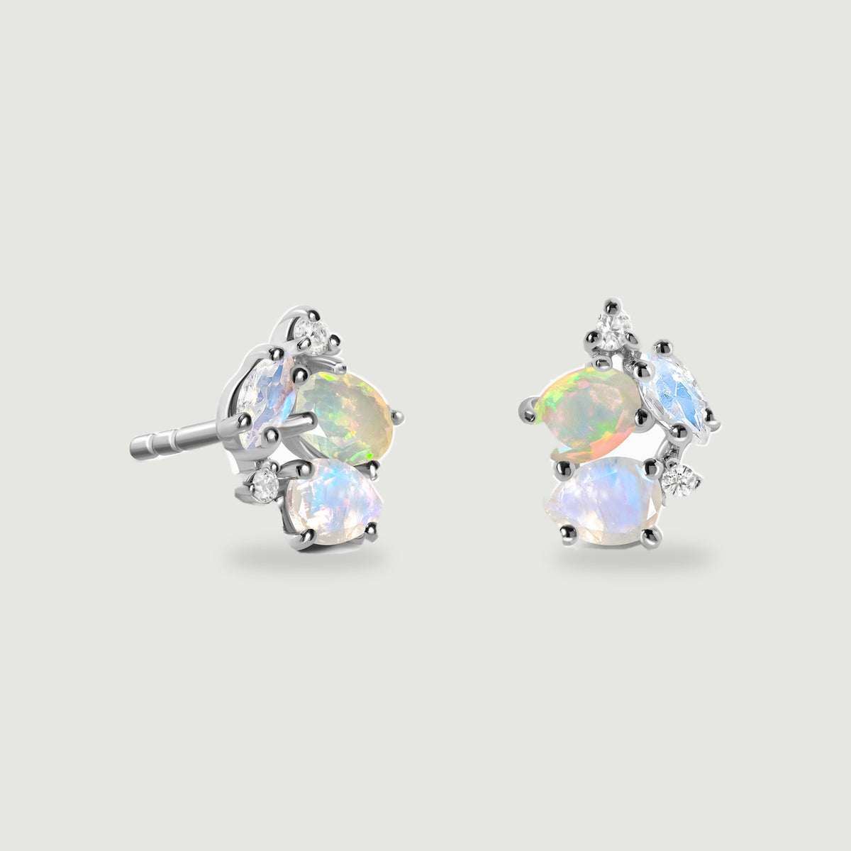 A sterling silver earring pair rests against light gray, with polished prongs surrounding opal and moonstone clusters.