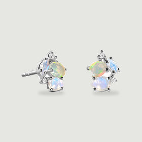 A sterling silver earring pair rests against light gray, with polished prongs surrounding opal and moonstone clusters.