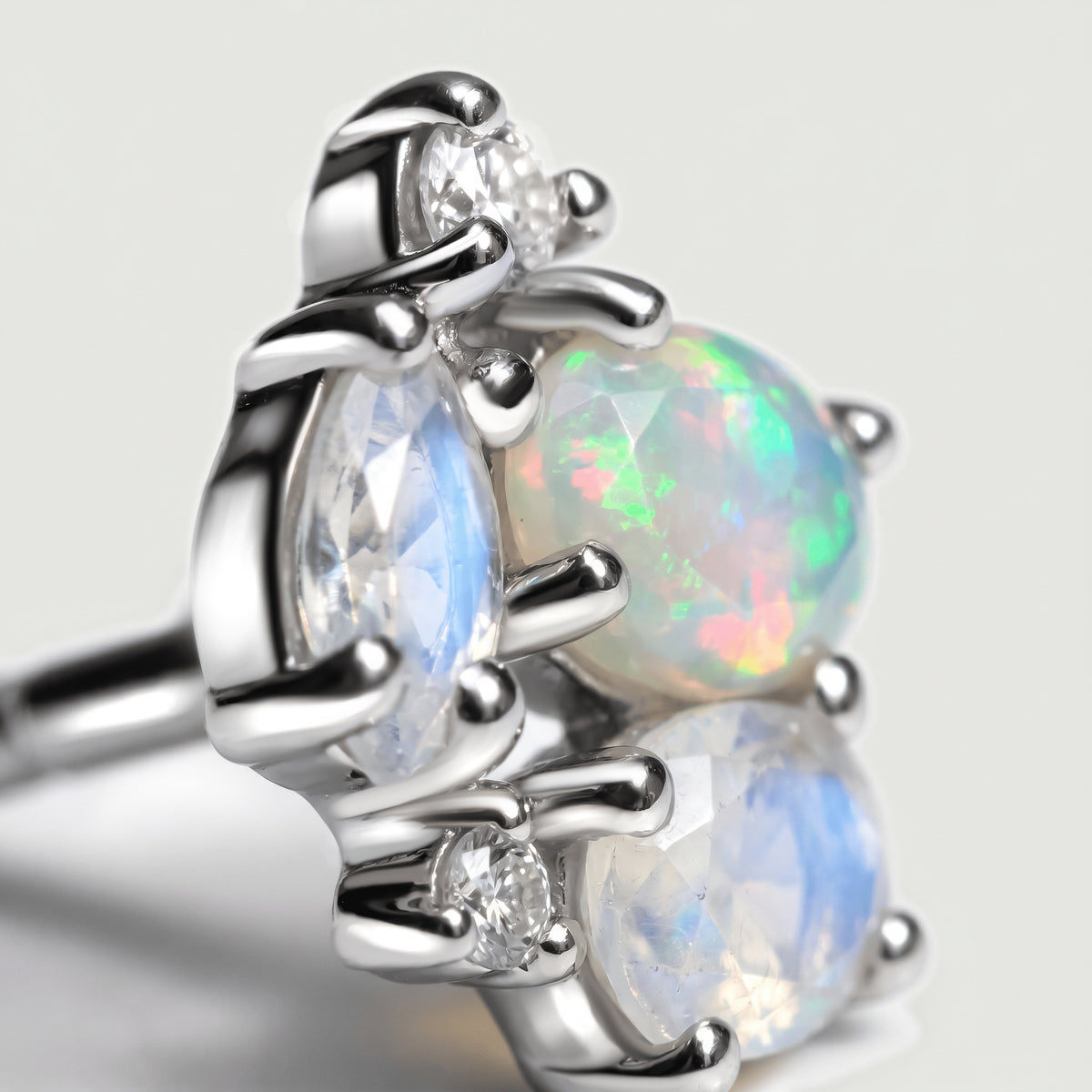 Polished silver prongs frame an opal and blue-flashing moonstones in an enlarged view of one stud.