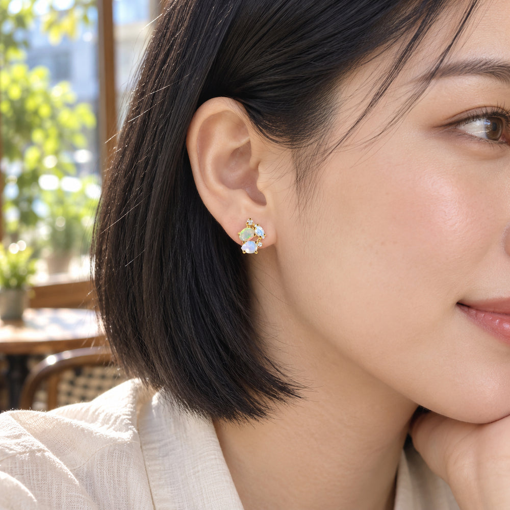 A woman with a black bob wears a yellow gold gemstone cluster stud beside a bright cafe window.