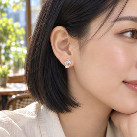A woman with a black bob wears a yellow gold gemstone cluster stud beside a bright cafe window.