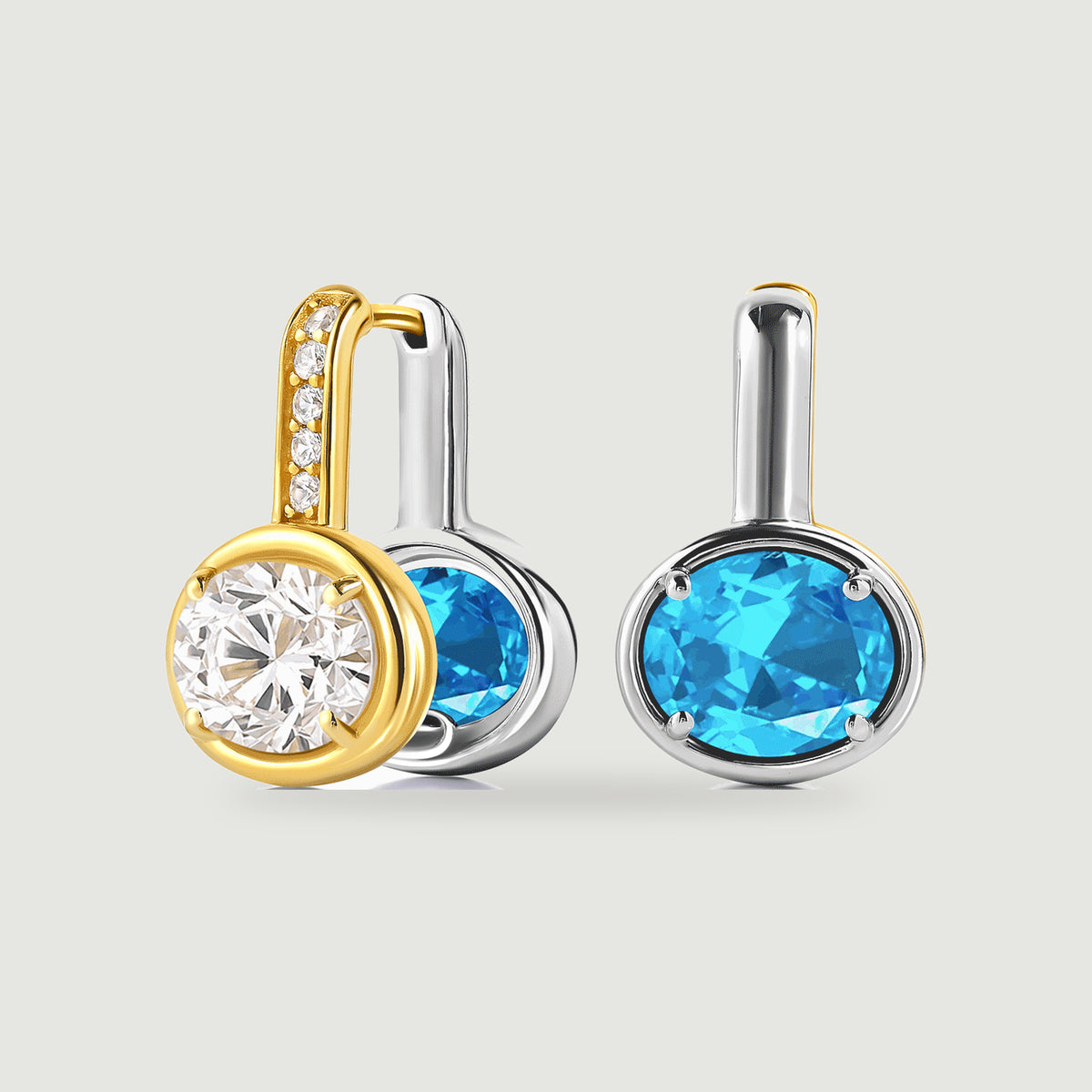 A pair of two-tone hoop earrings shows a clear oval stone on a gold-colored face and blue oval stones on silver-colored faces.