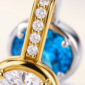 Clear stones line the gold-colored hoop above an oval setting, with a blue gemstone visible behind it.