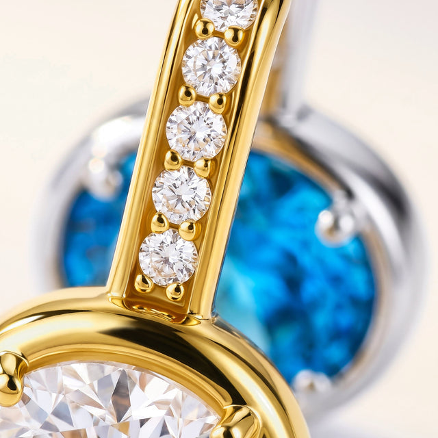 Clear stones line the gold-colored hoop above an oval setting, with a blue gemstone visible behind it.