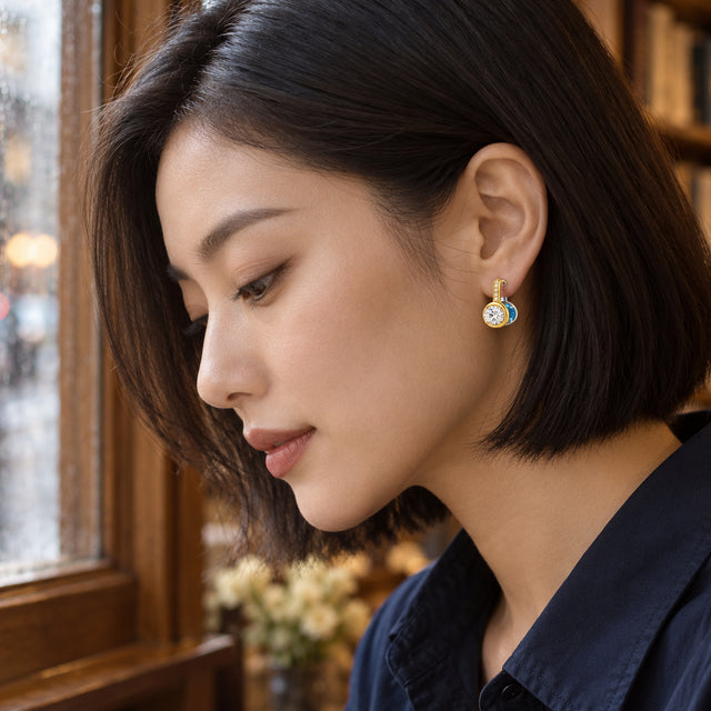 A woman with a straight dark bob wears the gold-colored face of a two-tone hoop earring beside a rain-speckled wooden window.