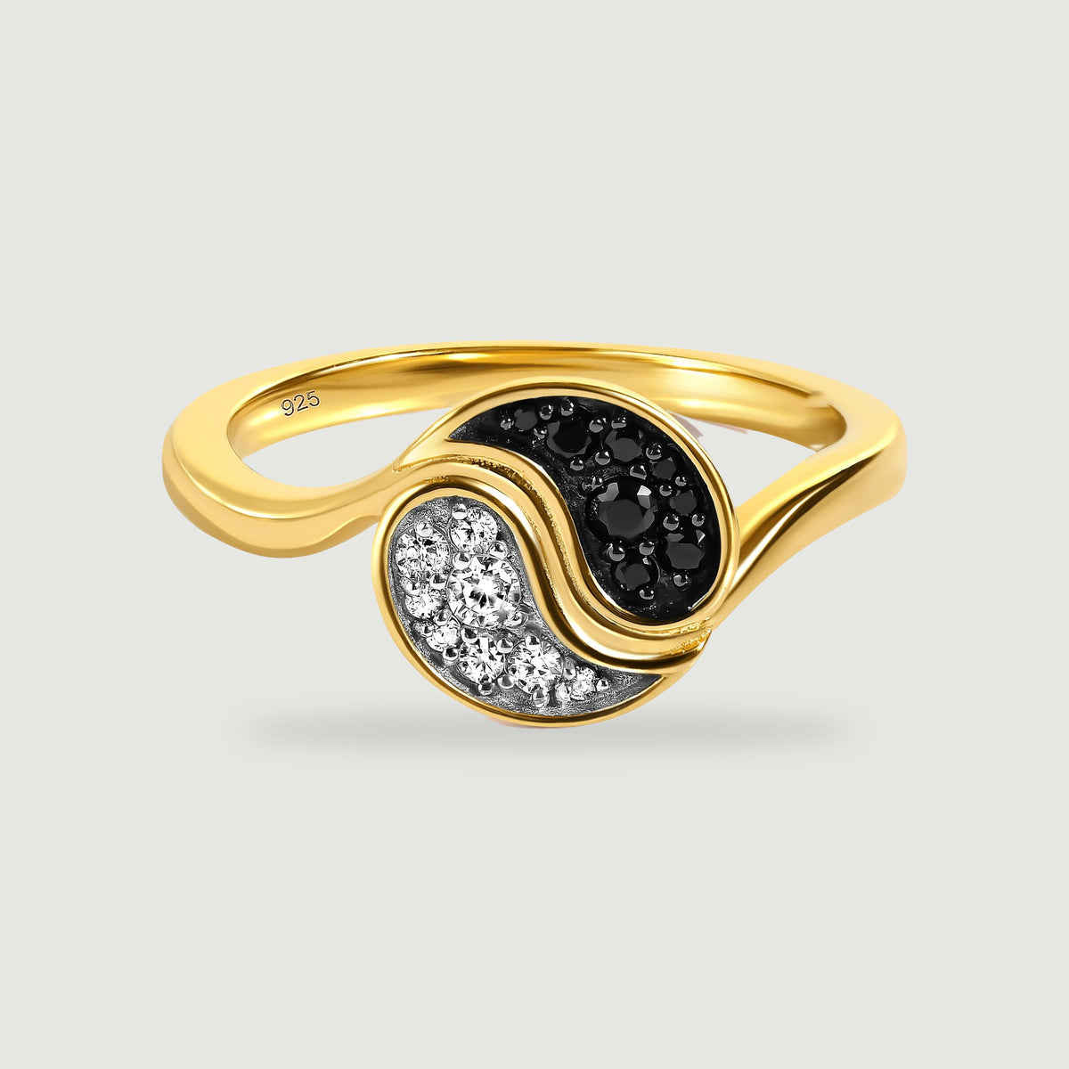 A yellow gold ring with curved sections of black and clear stones rests on a light gray surface.