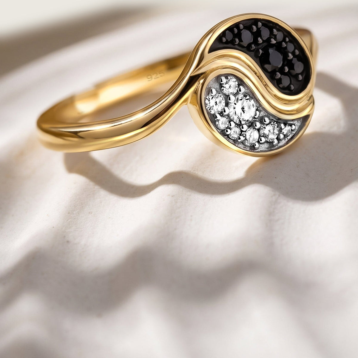 A yellow gold ring sits at an angle on a pale textured tabletop with a visible curved shadow.