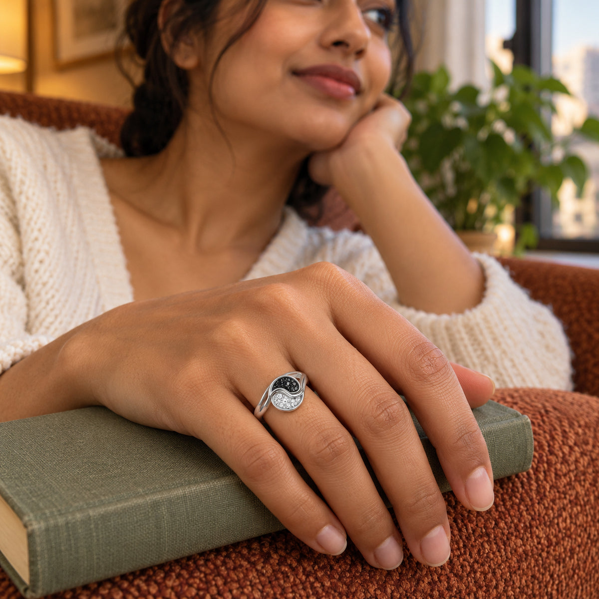 A silver ring with black and clear stones is worn on a hand resting on a green clothbound book.