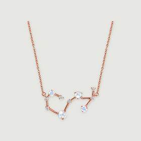 A rose gold chain connects to an open constellation pendant with pale round stones on a light gray surface.