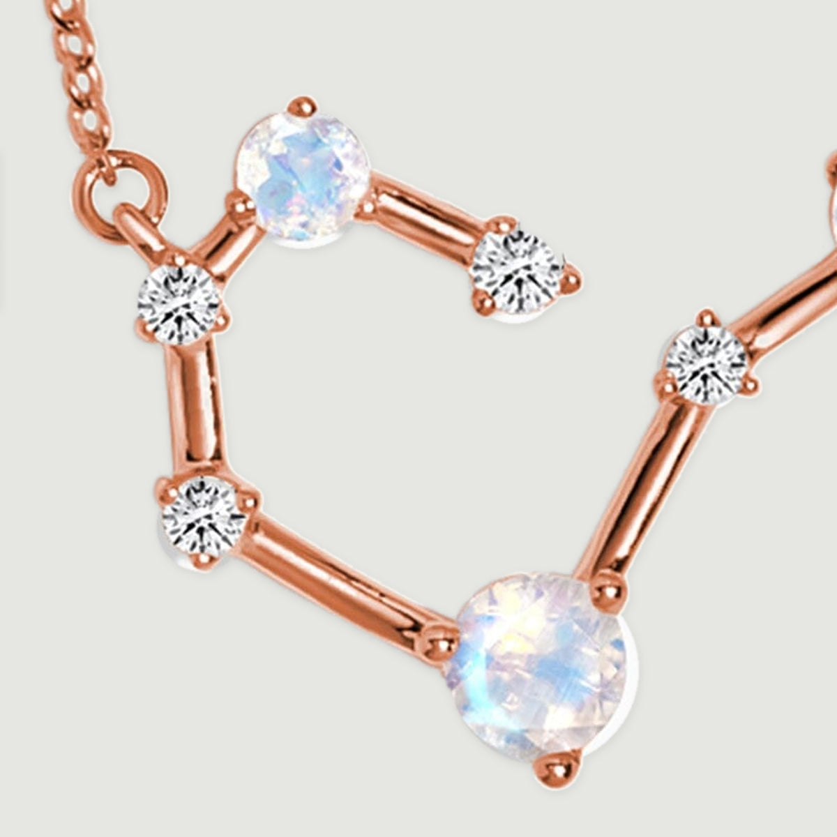 The left curve of a rose gold pendant shows a large pale stone, smaller clear stones, and polished connectors.