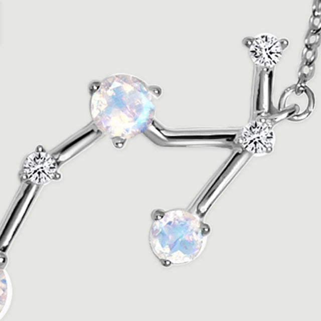 A close view of the silver pendant reveals a pale round stone, clear accents, and branching metal bars.