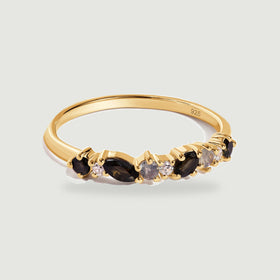 A yellow gold vermeil ring with black marquise stones and smaller round stones rests on a pale gray background.