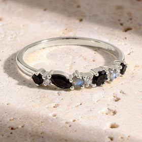The sterling silver ring lies on a textured cream stone surface with its row of dark and pale stones facing forward.
