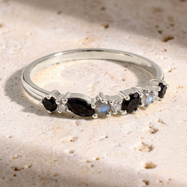 The sterling silver ring lies on a textured cream stone surface with its row of dark and pale stones facing forward.
