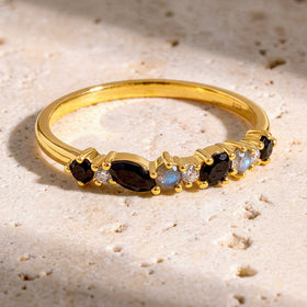 The yellow gold vermeil ring lies on a textured cream stone surface with its row of dark and pale stones facing forward.