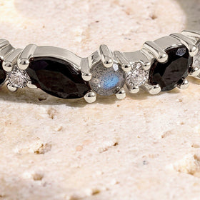 A close view shows the faceted black stones, pale round stones, and polished silver prongs against a cream stone surface.