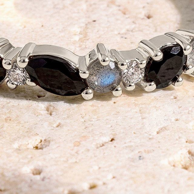 A close view shows the faceted black stones, pale round stones, and polished silver prongs against a cream stone surface.