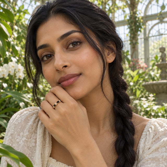 A woman with braided dark hair wears the yellow gold vermeil ring with her hand raised near her chin in a leafy greenhouse.