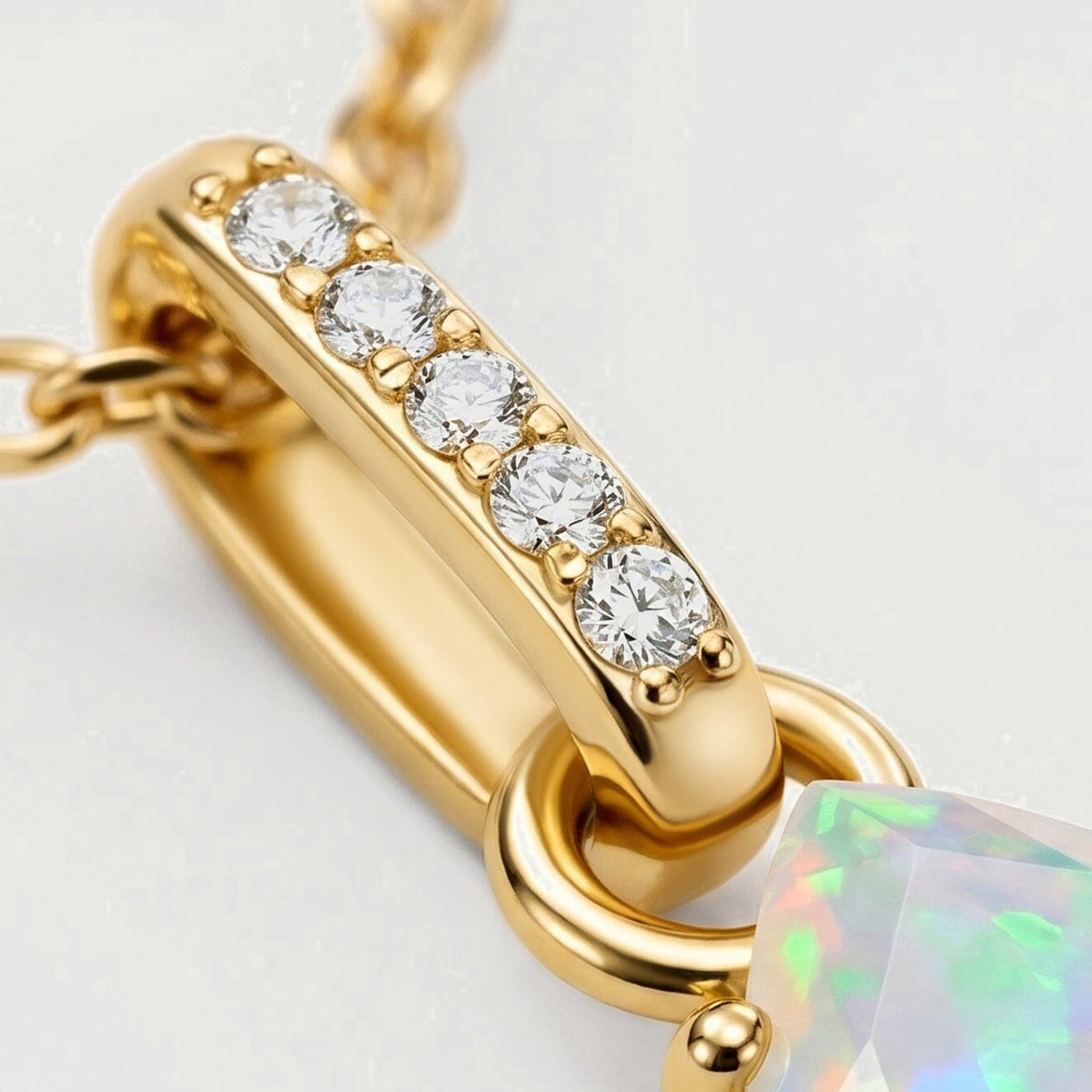 Five round clear stones sit in a yellow gold bail beside oval chain links and a polished connecting ring.