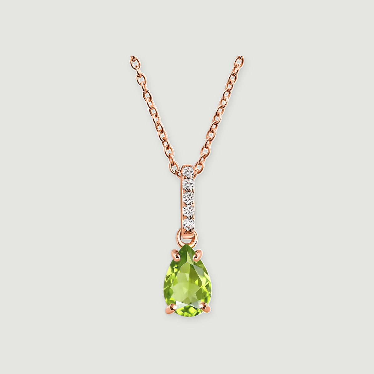 A rose gold vermeil chain supports a green peridot drop beneath a line of white stones on a light gray surface.