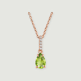 A rose gold vermeil chain supports a green peridot drop beneath a line of white stones on a light gray surface.