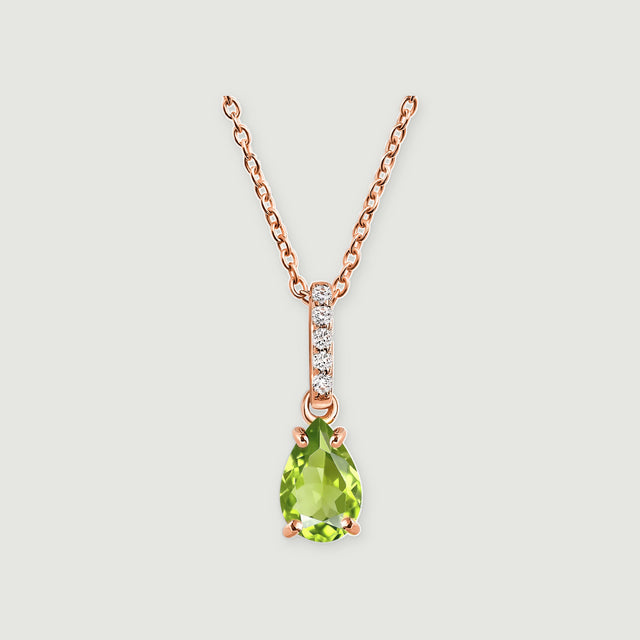 A rose gold vermeil chain supports a green peridot drop beneath a line of white stones on a light gray surface.