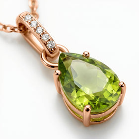 Rose gold prongs frame the pear-shaped peridot in an angled close-up with five white stones visible above it.