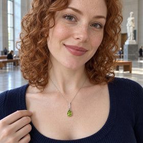 A red-haired woman in a navy top wears the sterling silver peridot necklace in a museum with stone walls and wooden benches.