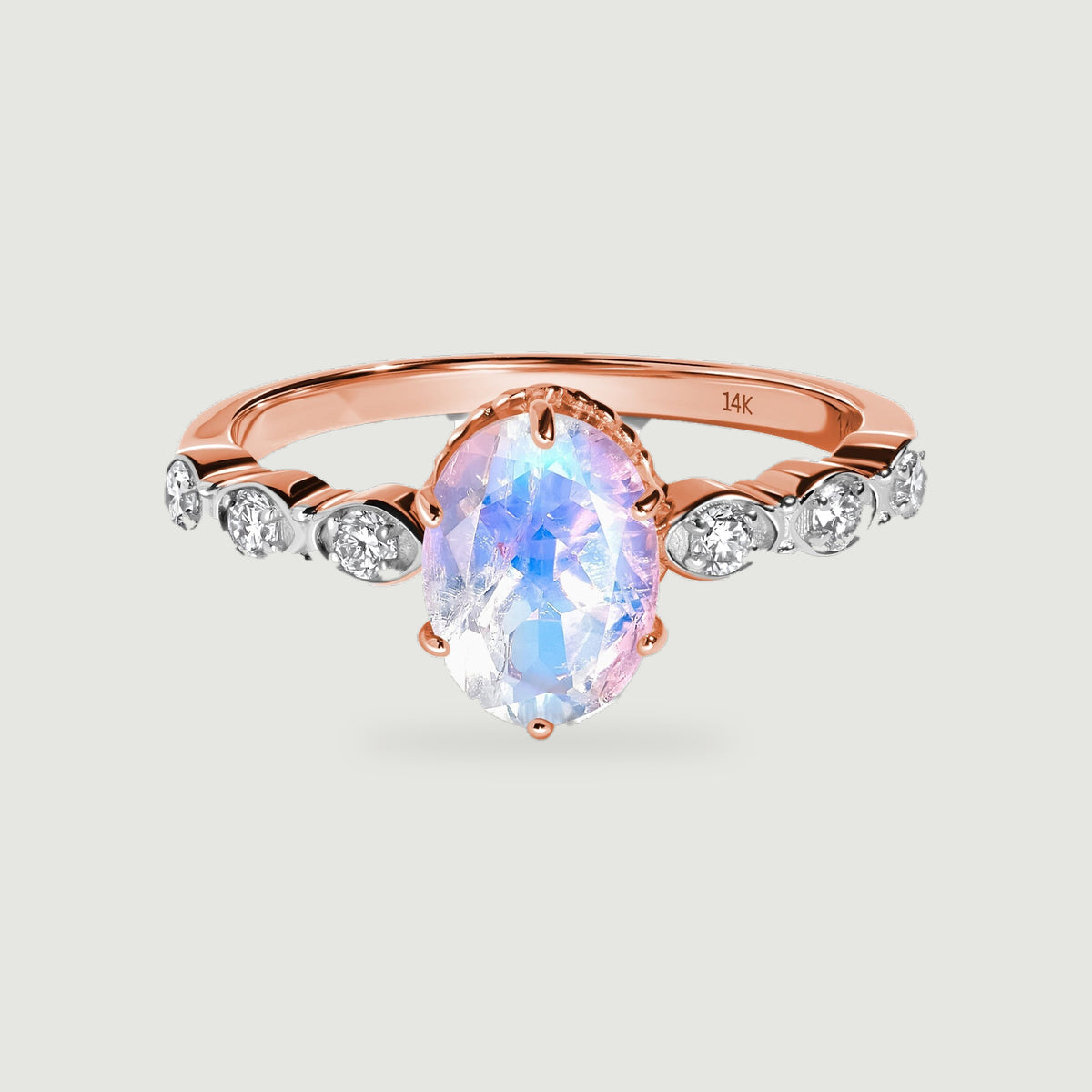 An oval moonstone with blue and lilac reflections sits between six round diamonds on a rose gold ring.