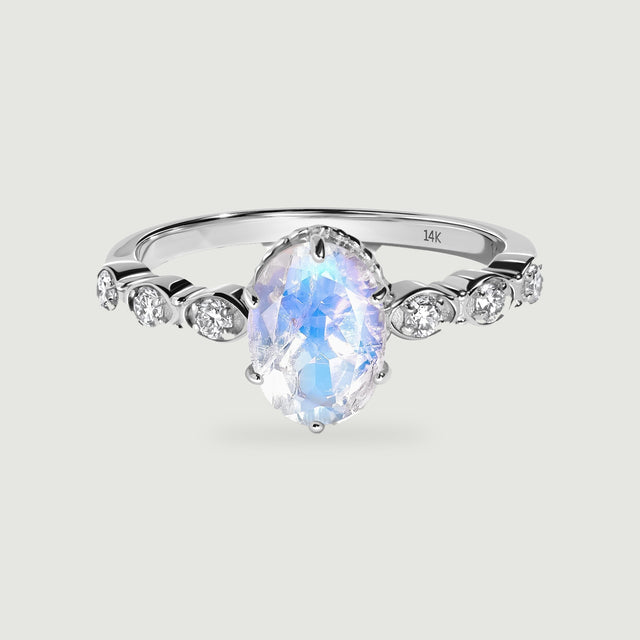 A white gold ring surrounds an oval faceted moonstone with three round diamonds on each shoulder.