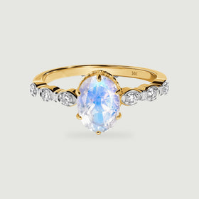 A yellow gold band holds an oval moonstone above six bright round diamond accents.