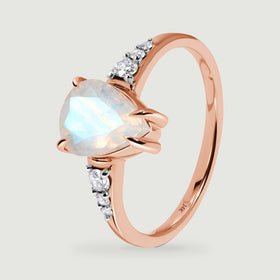 The rose gold band curves behind a faceted moonstone and bright diamond shoulder settings.