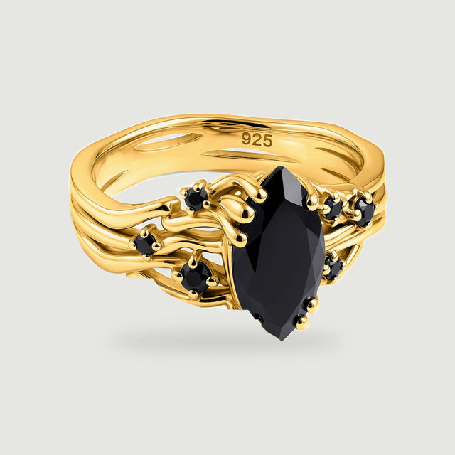 A yellow gold ring with a marquise black stone and six smaller black stones rests on a light gray background.