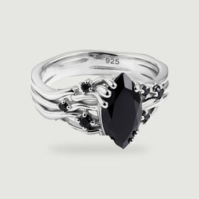 A silver ring with curved open bands and a pointed black center stone is shown against light gray.