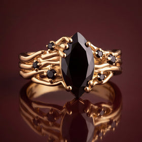 The yellow gold ring stands on a polished surface with its black stones reflected below.