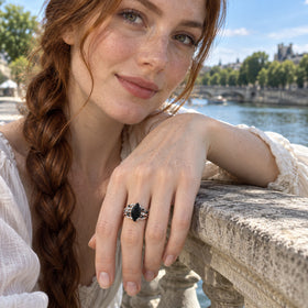 The silver ring is visible on a freckled hand resting on a stone balustrade above a river.