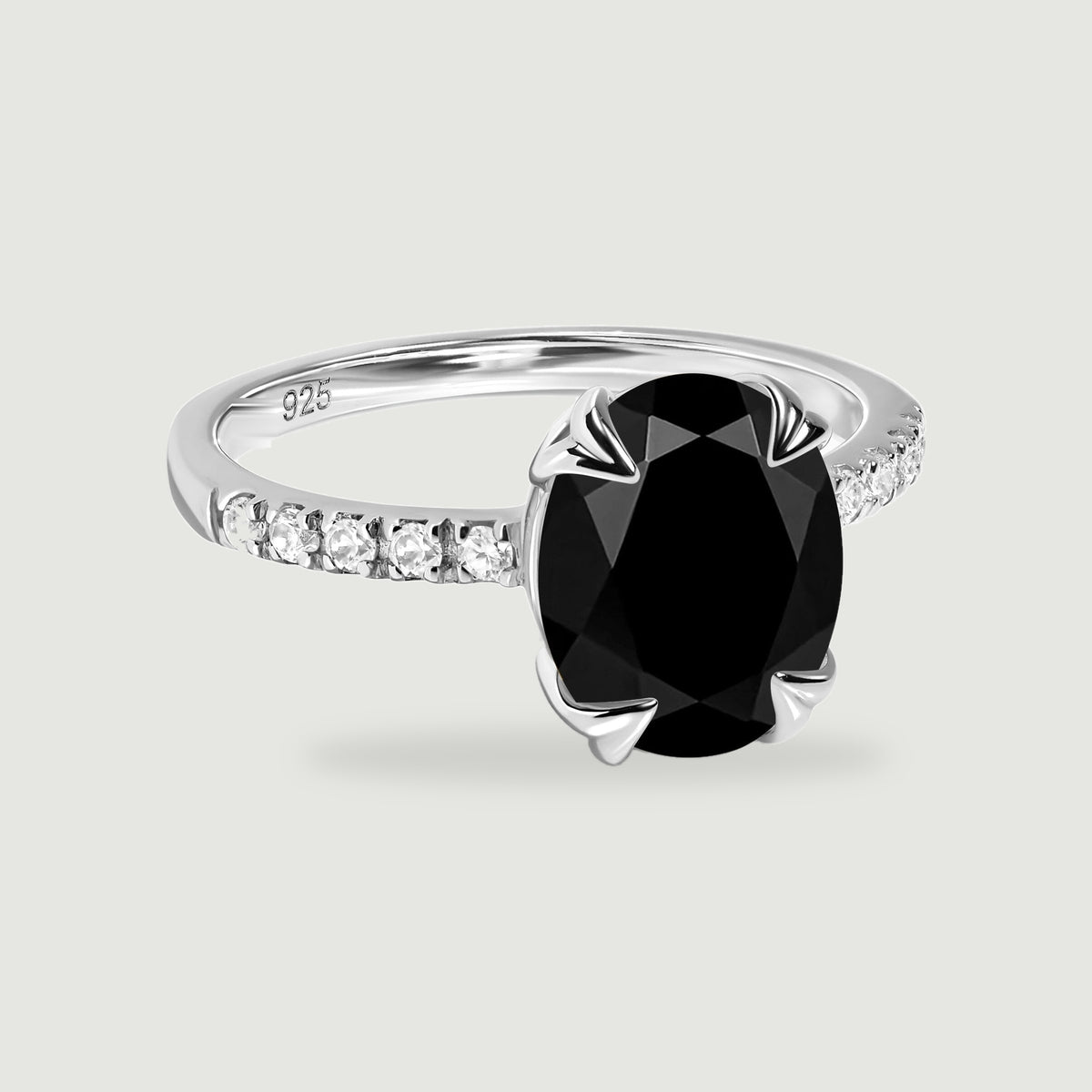 An oval faceted black stone sits in a silver ring with clear stones along both shoulders on a light gray background.