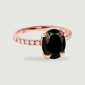 Four rose gold prongs hold an oval black stone above a slim band with clear accent stones on a light gray background.