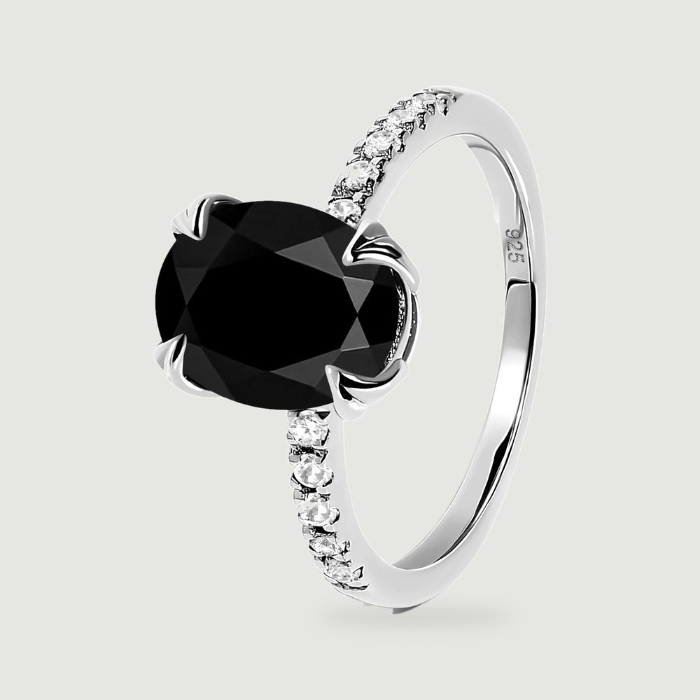 The silver ring is shown upright at an angle, revealing the faceted black stone and the curve of the band.
